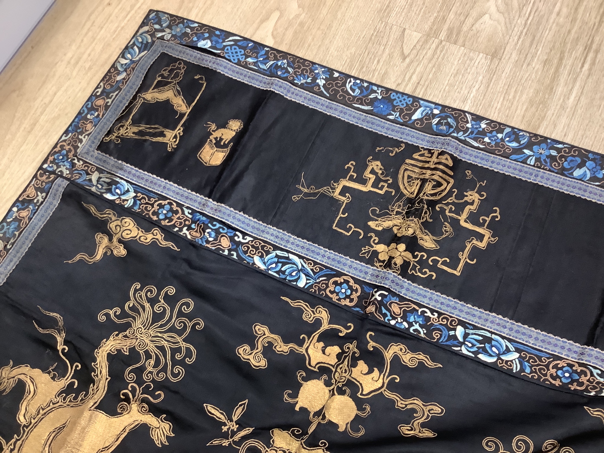 A 19th century Chinese dark blue ground panel, gilt thread embroidered with a pair of celestial dragons flying amongst precious objects, beneath a frieze, 95 x 95cm
